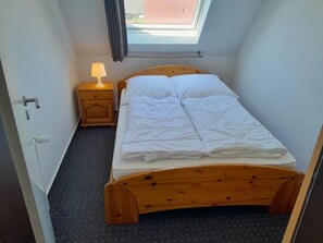 A single bed with a wooden frame, a nightstand with a lamp, and a skylight above. - NEW! Vacation Rental "Sound of the Sea" 4c (Dornum)