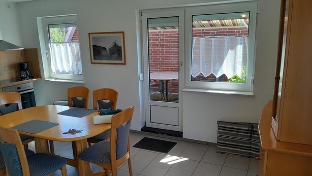 Een eetgedeelte met een tafel en stoelen, een keuken met een fornuis en spoelbak, en een deur naar een terras.