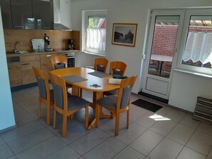 A modern kitchen with a dining area, including a table and chairs, a coffee maker, and a window with a view. - NEW! Vacation Rental "Sound of the Sea" 4c (Dornum)