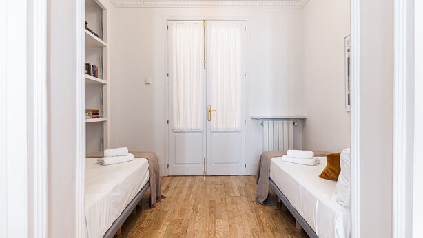 A narrow room with two beds, a white door, a radiator, and a small table. - Waou Sol XI - Short-Term Rental (Madrid)