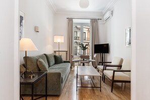 A modern living room with a sofa, coffee table, TV, and a view of a balcony with outdoor furniture. - Waou Sol XI - Short-Term Rental (Madrid)