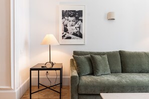 A living room with a green sofa, a small table with a lamp, and a framed picture on the wall. - Waou Sol XI - Short-Term Rental (Madrid)