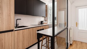 A modern kitchen with wooden cabinets, a black countertop, and a glass partition. - Waou Sol XI - Short-Term Rental (Madrid)