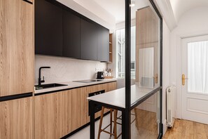 A modern kitchen with wooden cabinets, a black countertop, and a glass partition. - Waou Sol XI - Short-Term Rental (Madrid)