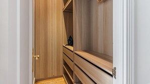 A walk-in closet with wooden shelving and a single hanging garment. - Waou Sol XI - Short-Term Rental (Madrid)