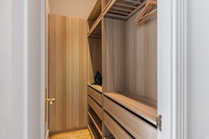 A walk-in closet with wooden shelving and a single hanging garment. - Waou Sol XI - Short-Term Rental (Madrid)