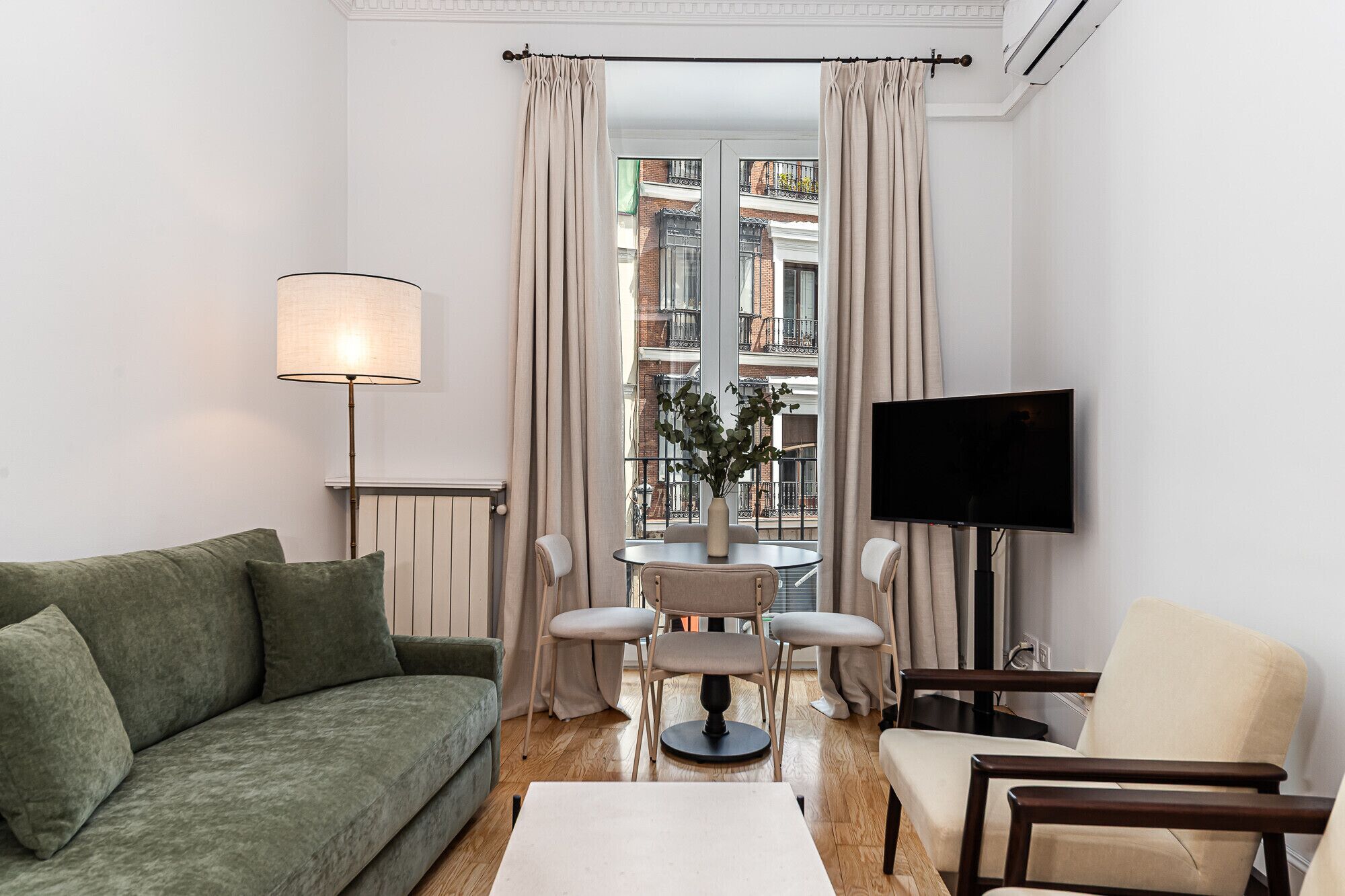A living room with a sofa, a table with chairs, a TV, and a window with curtains.