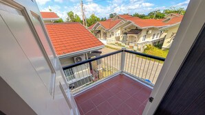 Un balcon orné de tuiles rouges, une porte blanche et une vue sur les maisons voisines, dont les toits sont également rouges.