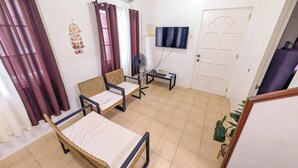 Une pièce comprenant un lit, deux chaises, un téléviseur, un climatiseur, un ventilateur et une porte.