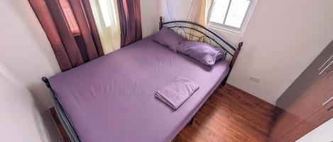 A single bed with a metal frame, a window with curtains, and a wooden floor.