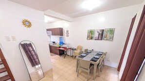 Un coin repas avec une table dressée pour six personnes, une cuisine en arrière-plan et un escalier menant à un autre niveau.