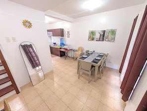 Comedor con una mesa lista para seis comensales, cocina al fondo y una escalera que sube a otro nivel.