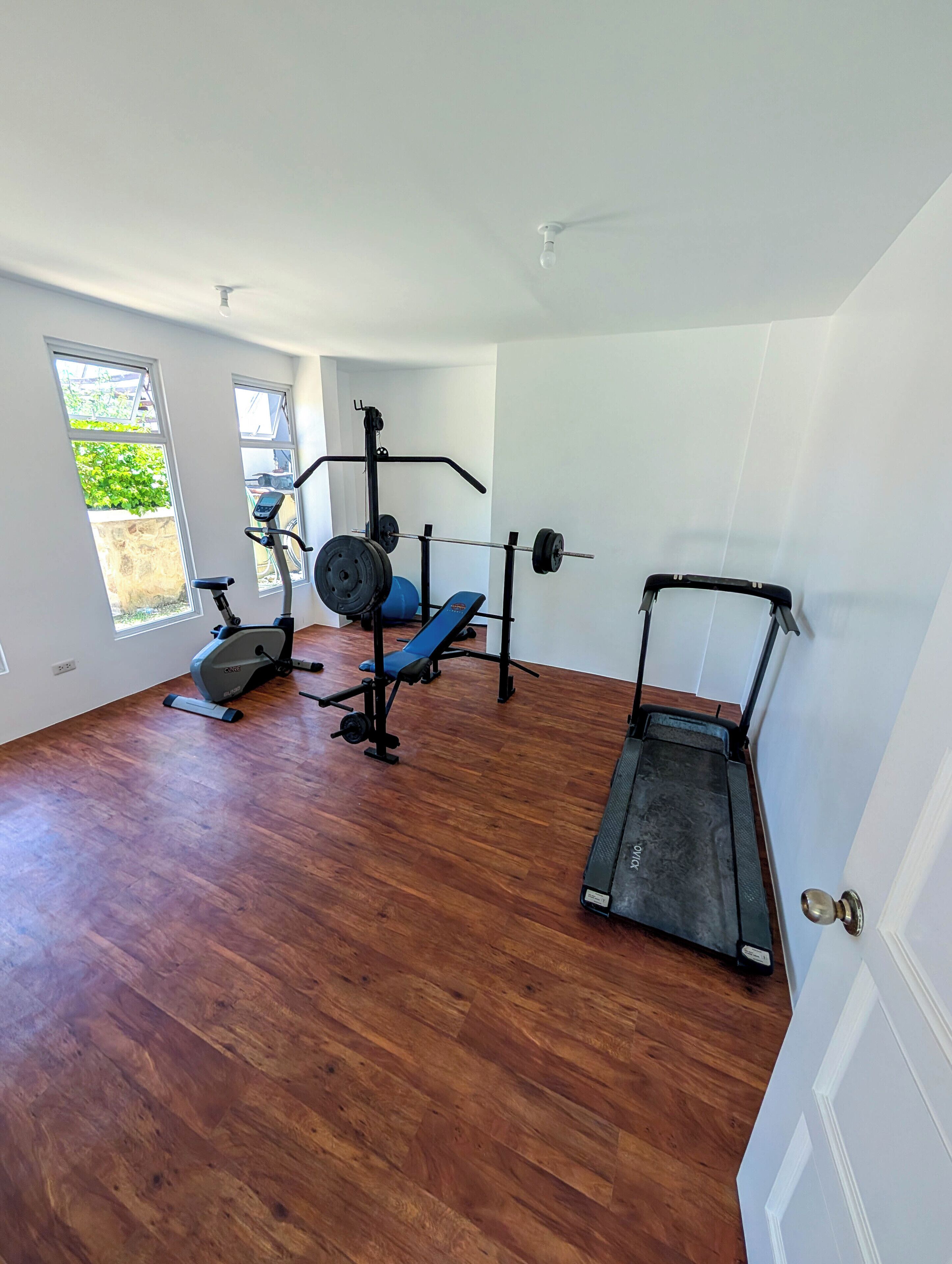 Un gimnasio con equipo de ejercicio, una cinta de correr y una ventana que ofrece vistas a la vegetación.
