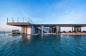 A modern infinity pool with a glass balustrade, lounge chairs, and a contemporary building structure. - Pattaya Central Excellent 1 Bed Room Near Beach (Pattaya)