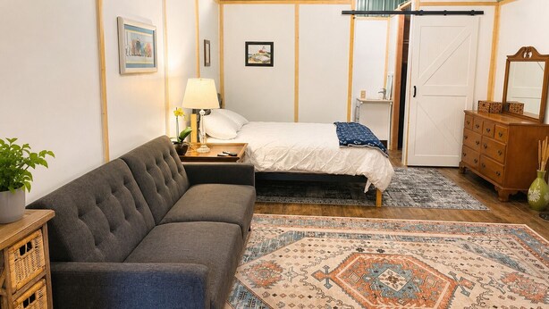 Um quarto com uma cama, um sofá, uma cômoda, um abajur e um tapete.