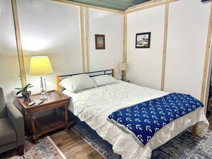 Un dormitorio con cama, mesitas de noche, lámpara, planta y alfombra.