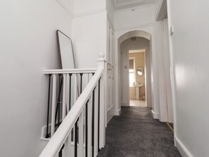 Ein Flur mit einer weißen Treppe, einer Tür zu einem Badezimmer und einem dunklen Teppichboden.