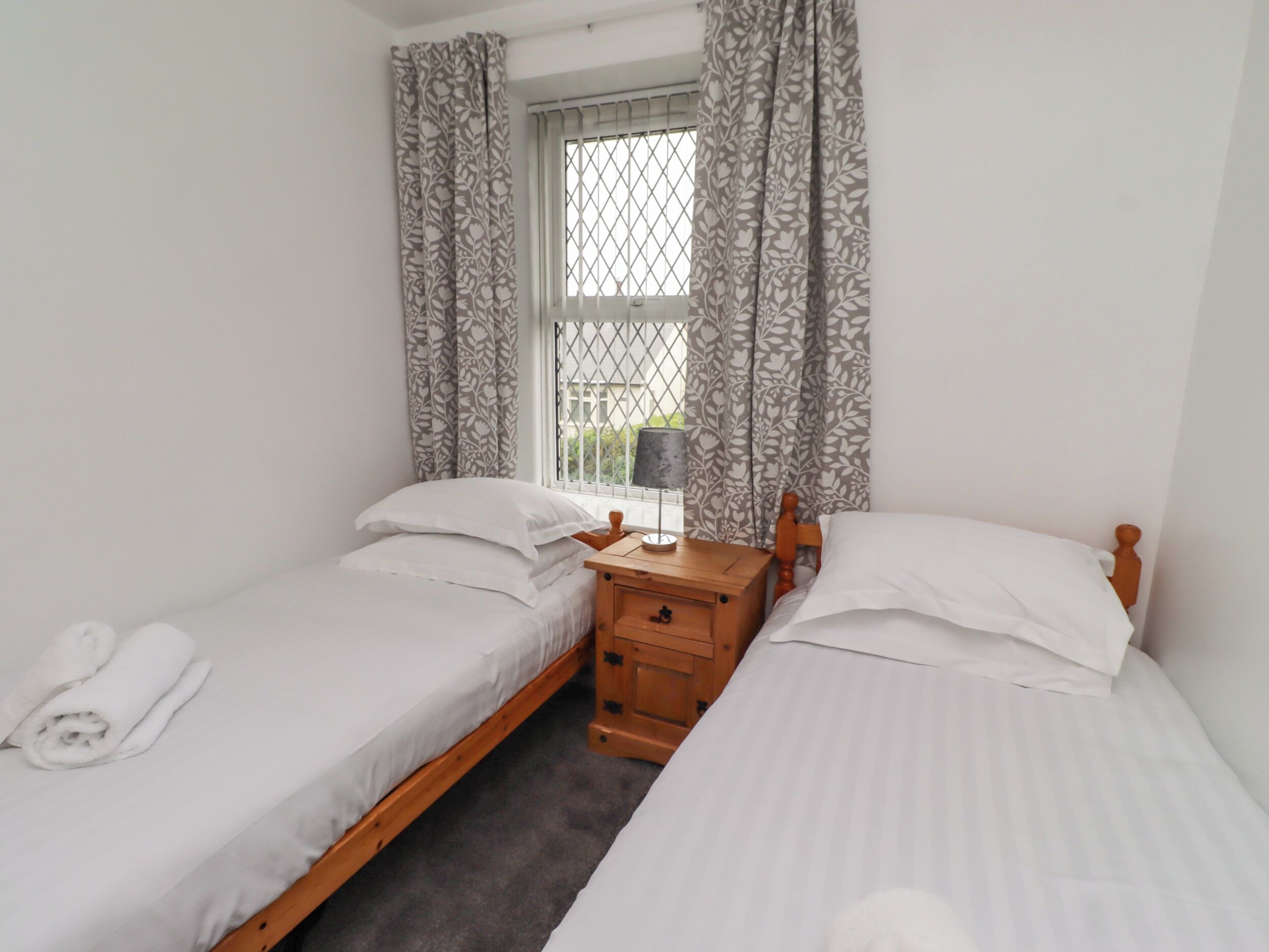 Une chambre double avec deux lits simples, une table de chevet en bois, une fenêtre avec des rideaux et une vue sur la verdure environnante.