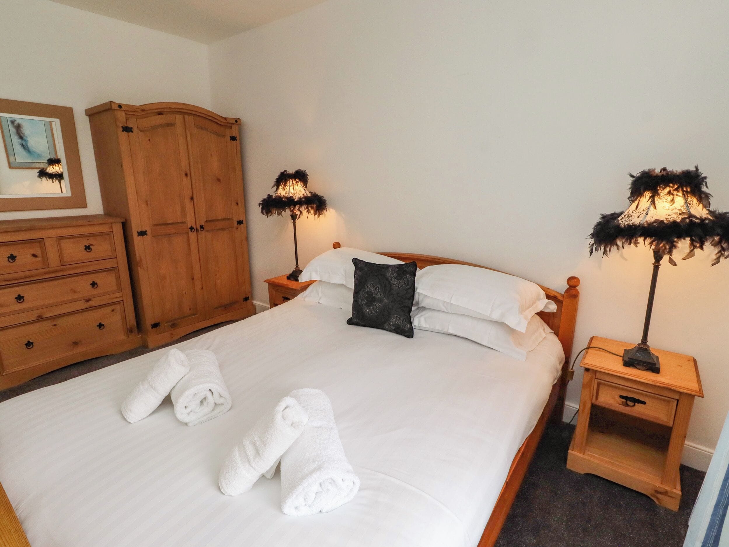 A neatly made bed with white linens and rolled towels, wooden nightstands with lamps, and a wooden wardrobe.