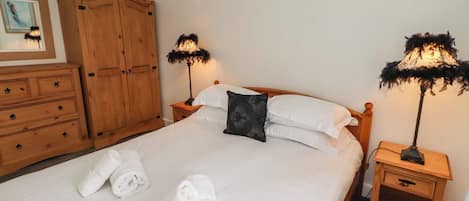 Ein ordentlich bezogenes Bett mit weißen Leinen und zusammengerollten Handtüchern, Nachttische aus Holz mit Lampen und ein Holzschrank.
