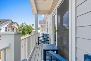 Un balcon couvert avec une table et des chaises, des balustrades blanches et une vue sur les maisons voisines.