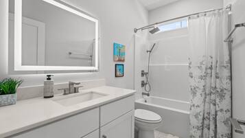 A modern bathroom with a large mirror, a sink, a toilet, and a shower.