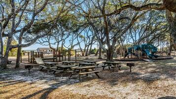 A park with picnic tables, playground equipment, and trees.
