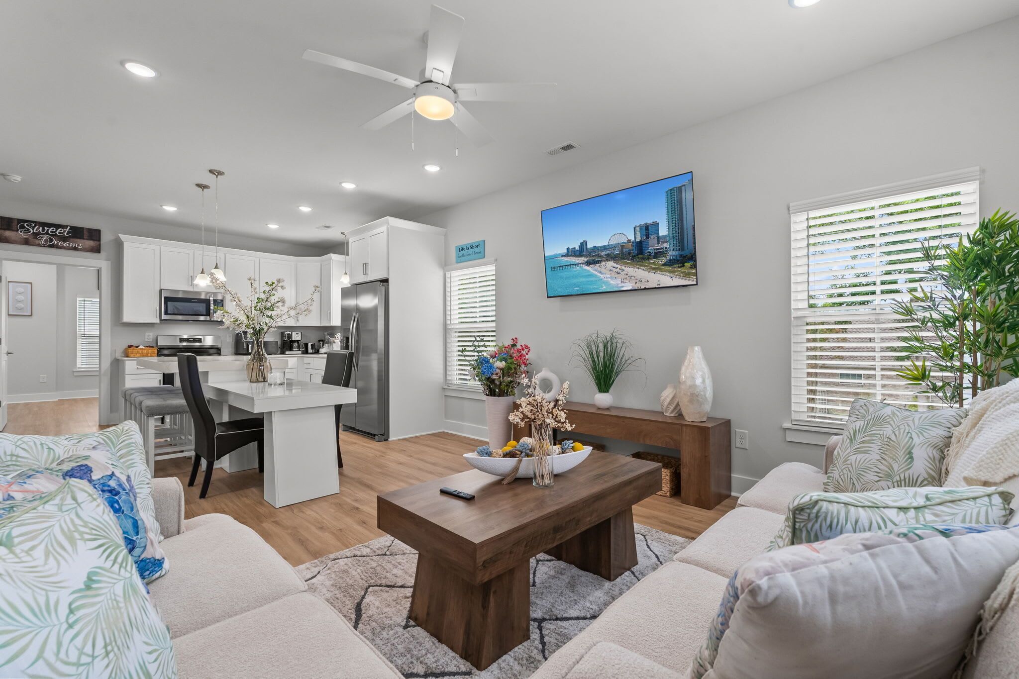 A modern living room with a dining area, kitchen, and a large window with blinds.