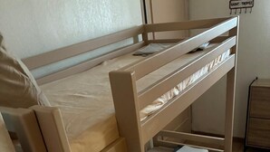 Un lit superposé avec un matelas et un oreiller, une petite armoire et un panneau mural.