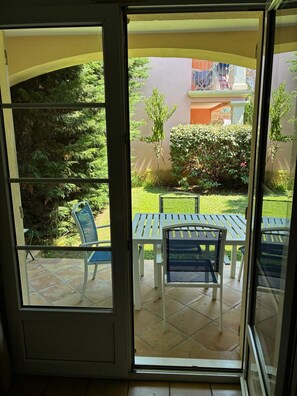 Porta de vidro deslizante aberta que dá para um espaço de pátio externo com mesa e cadeiras.