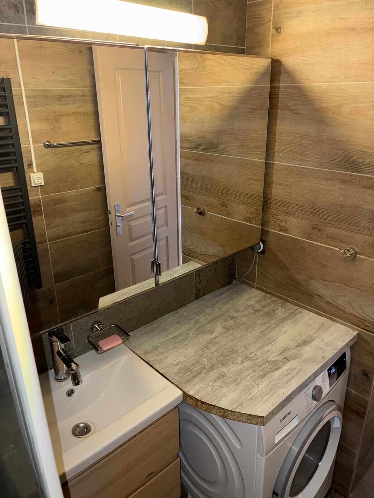 A compact bathroom with a sink, mirror, and washing machine.