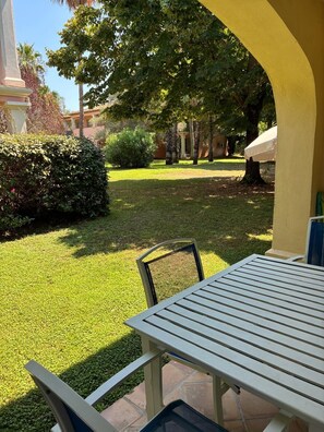 Een terras met een tafel en stoelen, omringd door een verzorgd gazon en bomen.