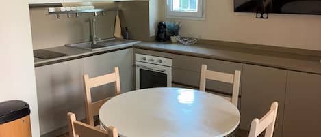 A modern kitchen with a dining table and chairs, a hanging light fixture, and a flat-screen TV mounted on the wall.