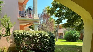Une terrasse extérieure avec une table et des chaises, entourée d’une pelouse bien entretenue et d’un bâtiment doté d’un balcon.