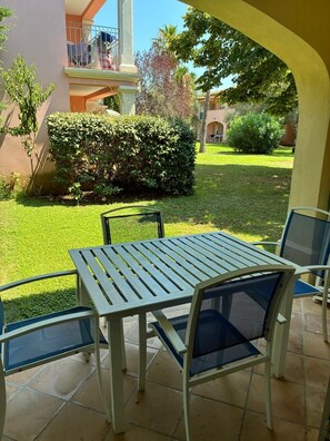 An outdoor patio with a table and chairs, surrounded by a well-maintained lawn and a building with a balcony. - Beautiful, air-conditioned one-bedroom apartment with a fully equipped kitchen, sleeps 6, with a pool (Grimaud)