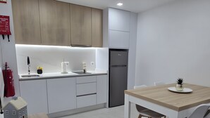 A modern kitchen with white cabinets, a built-in oven, and a dining area with a wooden table and chairs. - Casa da Lota: House with Large Terrace, Sea and Lota View (Vieira de Leiria)
