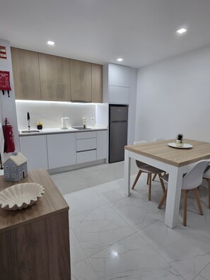 A modern kitchen with white cabinets, a built-in oven, and a dining area with a wooden table and chairs. - Casa da Lota: House with Large Terrace, Sea and Lota View (Vieira de Leiria)
