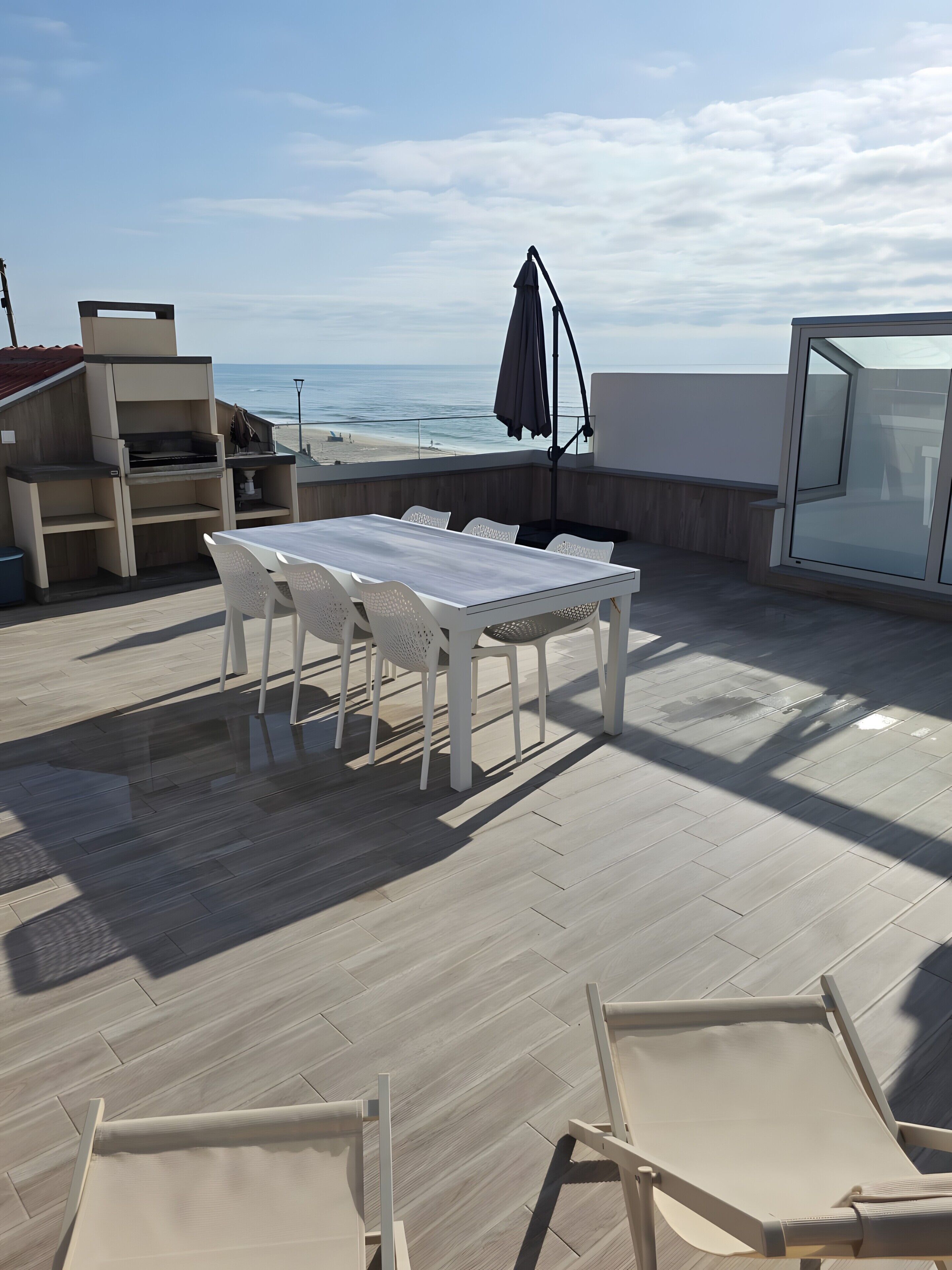 Une terrasse sur le toit, avec une table et des chaises, un barbecue et une vue sur l’océan.