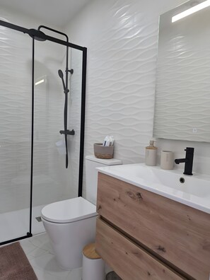 A modern bathroom with a glass shower enclosure, a white toilet, a wooden vanity, and a mirror above the sink. - Casa da Lota: House with Large Terrace, Sea and Lota View (Vieira de Leiria)