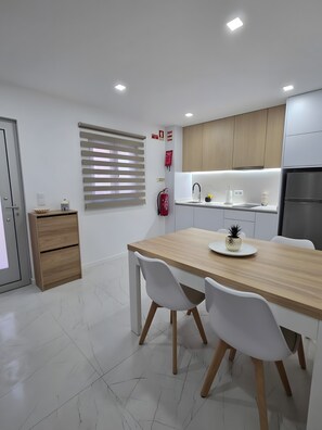 Une cuisine moderne avec des meubles en bois, un réfrigérateur en acier inoxydable et un coin repas comprenant une table en bois et des chaises blanches.