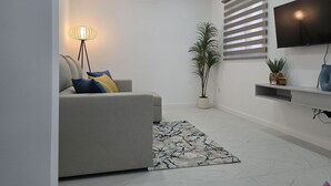 A modern living room with a sofa, a floor lamp, a potted plant, a flat-screen TV, and a patterned rug. - Casa da Lota: House with Large Terrace, Sea and Lota View (Vieira de Leiria)