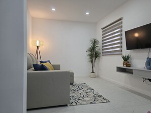 A modern living room with a sofa, a floor lamp, a potted plant, a flat-screen TV, and a patterned rug. - Casa da Lota: House with Large Terrace, Sea and Lota View (Vieira de Leiria)