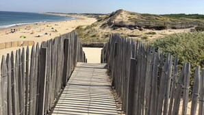 Una pasarela de madera que conduce a una playa con un sendero arenoso y una valla de madera a un lado.