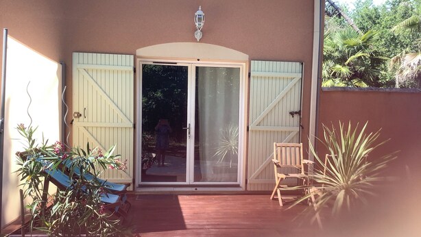 Un espacio al aire libre cubierto con puerta corredera de vidrio, un banco de madera y plantas en macetas.