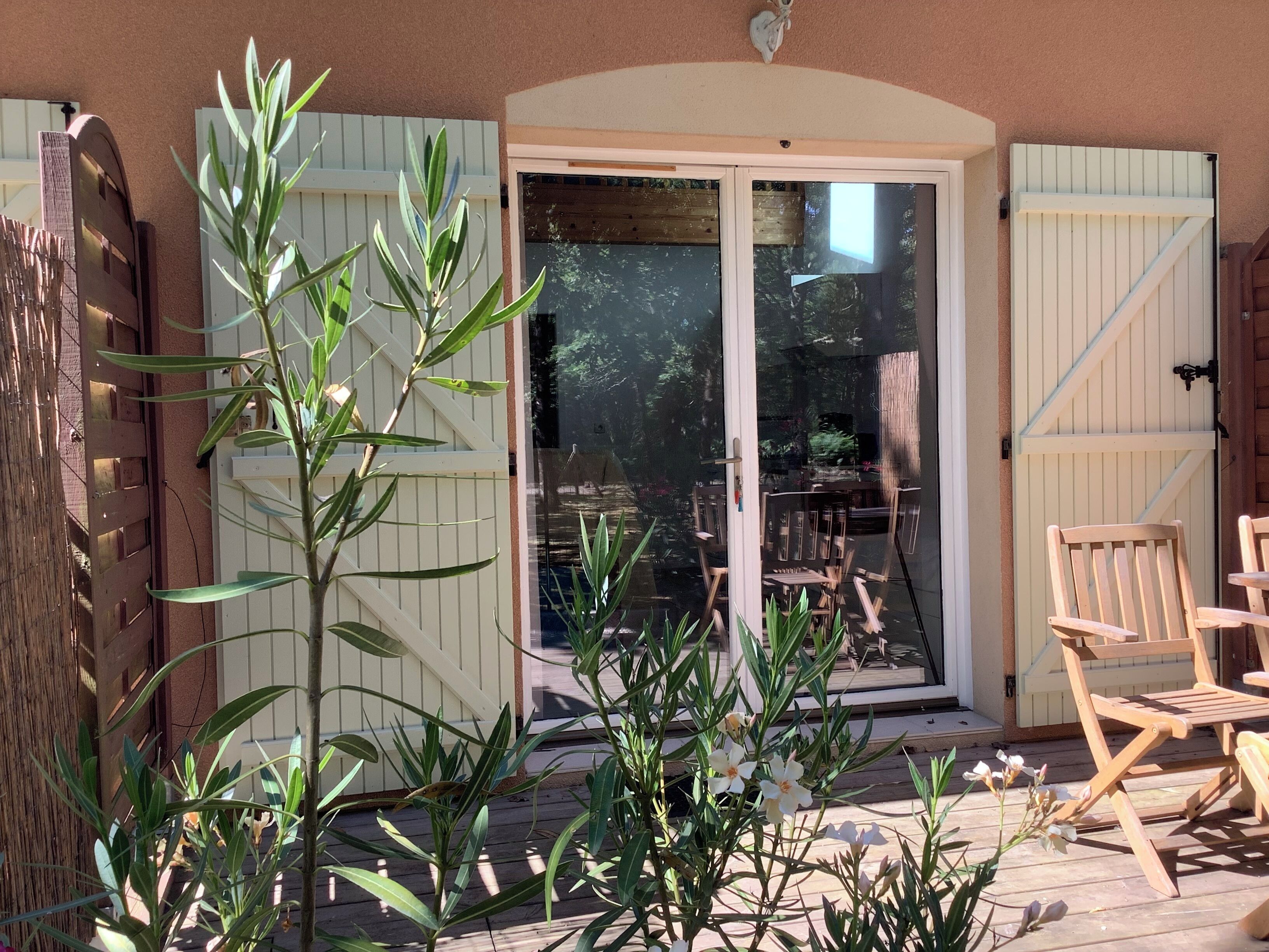 Una terraza de madera con mobiliario exterior, una puerta corrediza de vidrio y una cerca blanca.