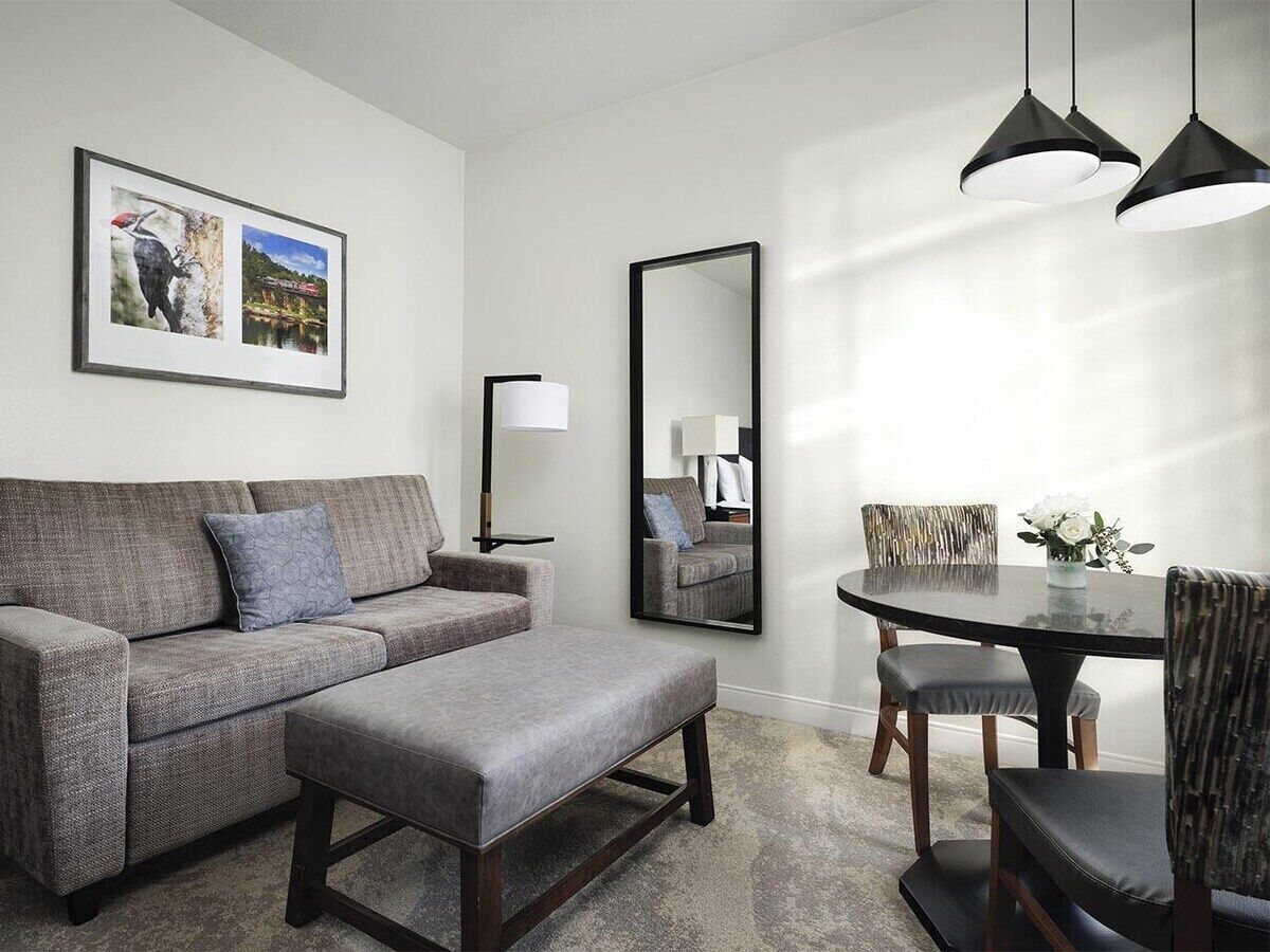 A modern living room with a sofa, ottoman, dining table, chairs, a mirror, and pendant lights.
