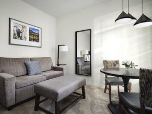 Ein modernes Wohnzimmer mit einer Couch, einem Hocker, einem Esstisch, Stühlen, einem Spiegel und Pendelleuchten.