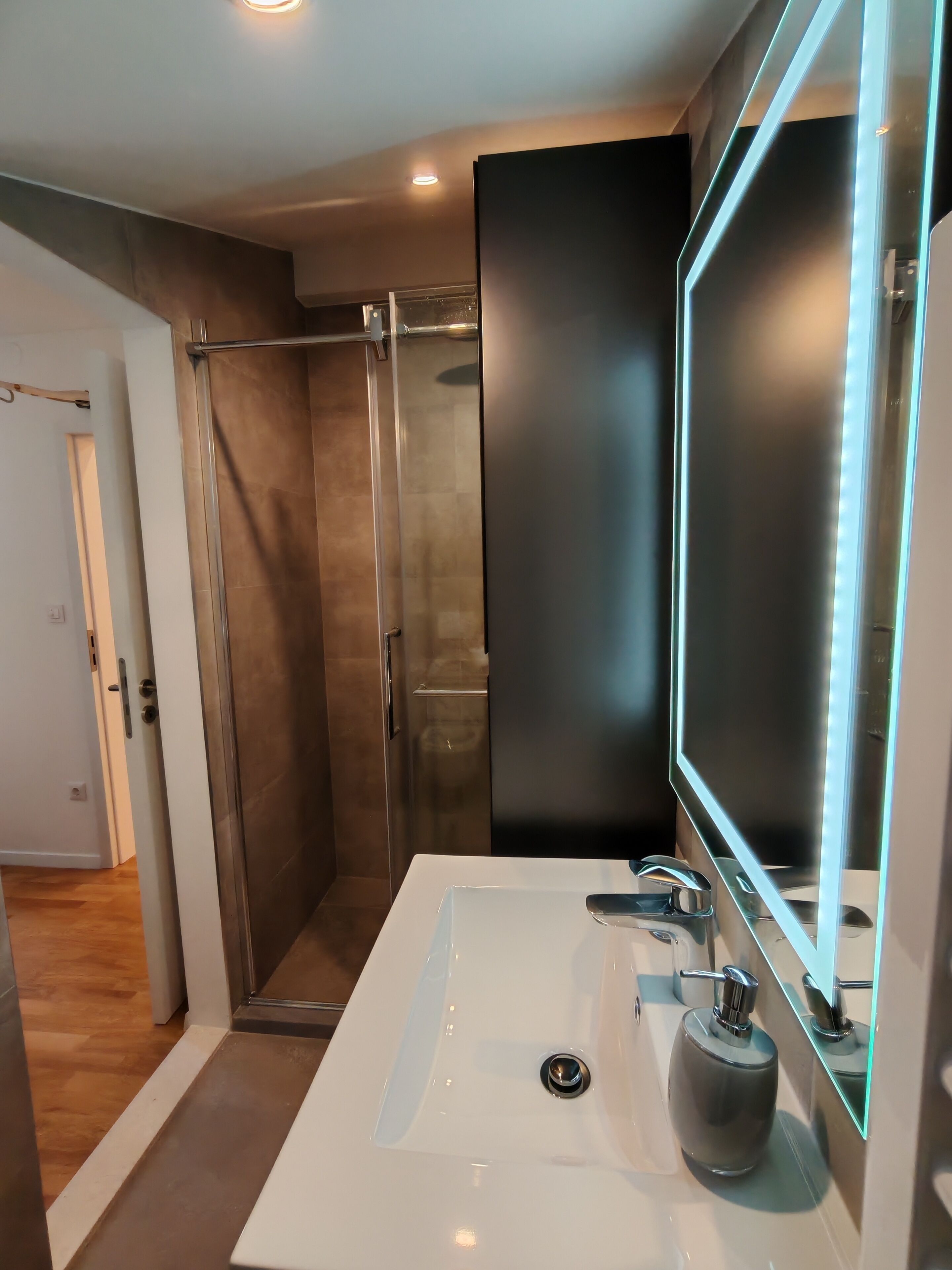 A modern bathroom with a large mirror, a white sink, and a glass shower enclosure.