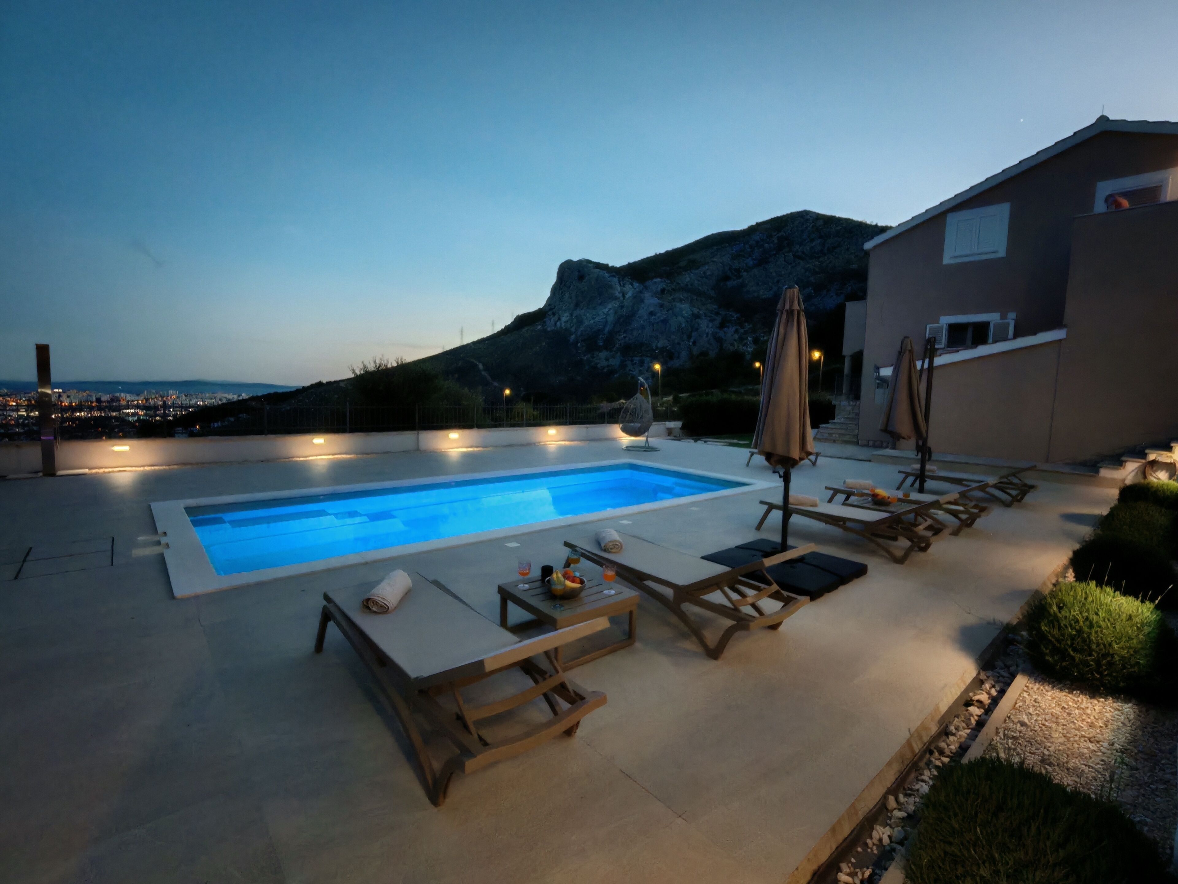 A swimming pool with lounge chairs and umbrellas, a view of the sea, and a building in the background.