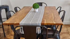 Et spisebord med træbordplade, omgivet af sorte stole, en lille potteplante og en grå dug. Tre billeder hænger på væggen over.